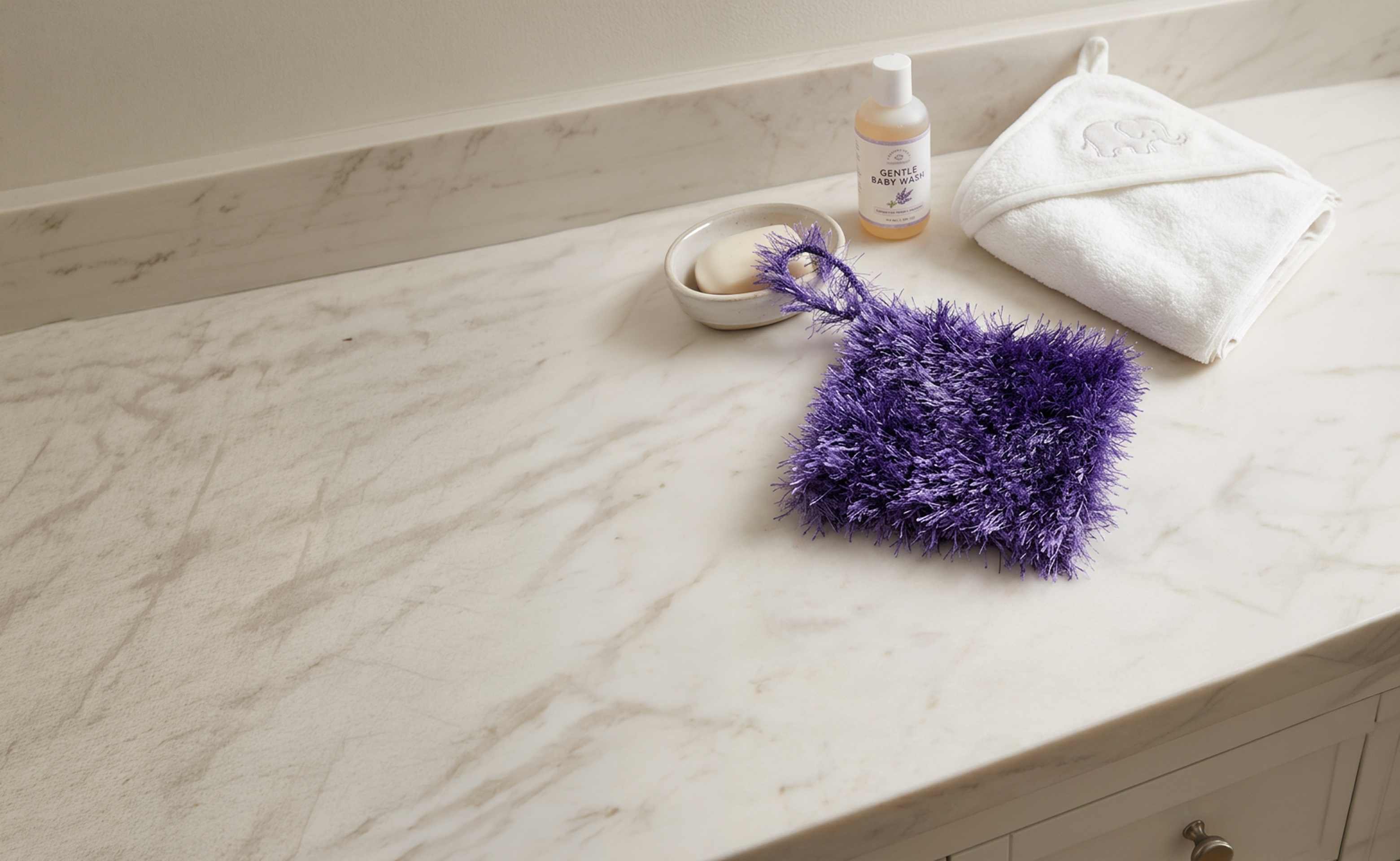 Green and purple Loofi Baby scrubbers laid together on a marble counter with gray subway tile backsplash
