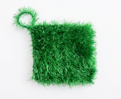 Green textured loofah scrubber with a hanging loop, laid flat on a white background